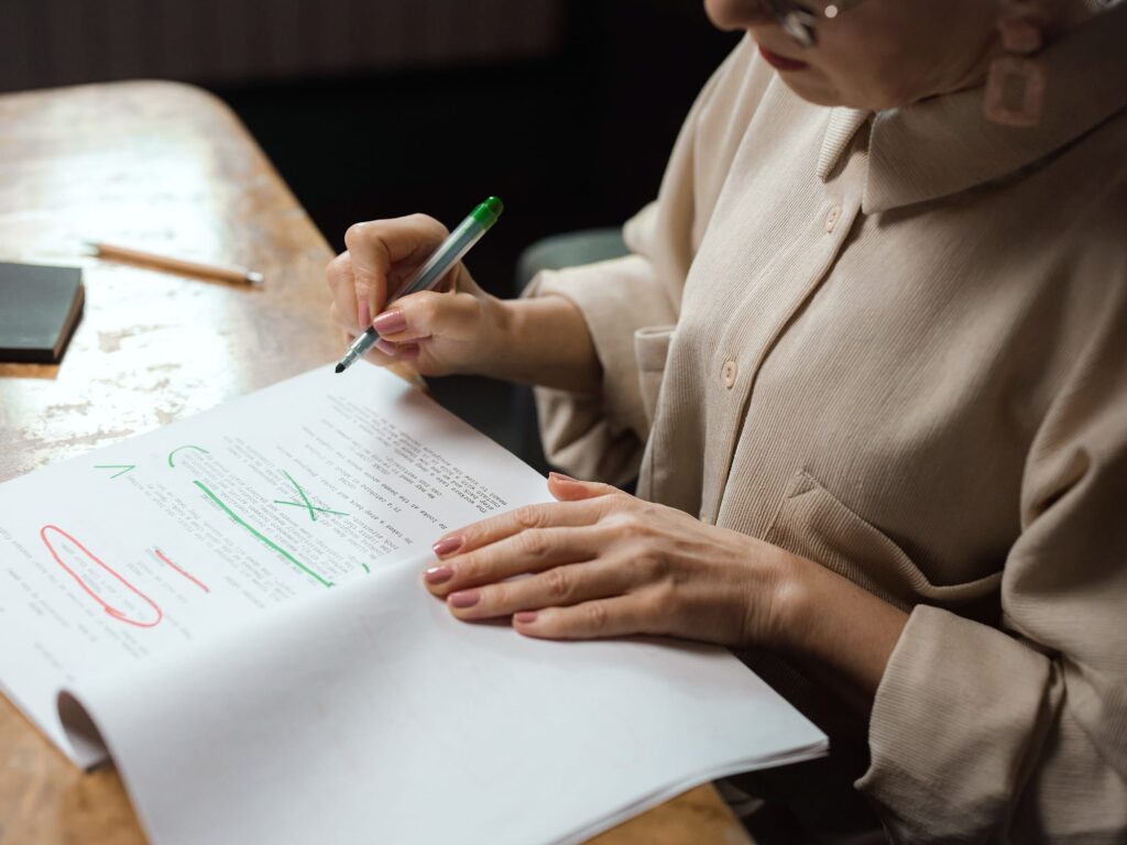 An editor marks up a printed draft with a green pen, red corrections circled on the page.
